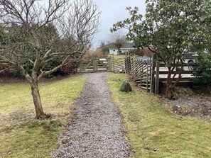 A gravel path leading to a wooden gate, surrounded by grass and trees.