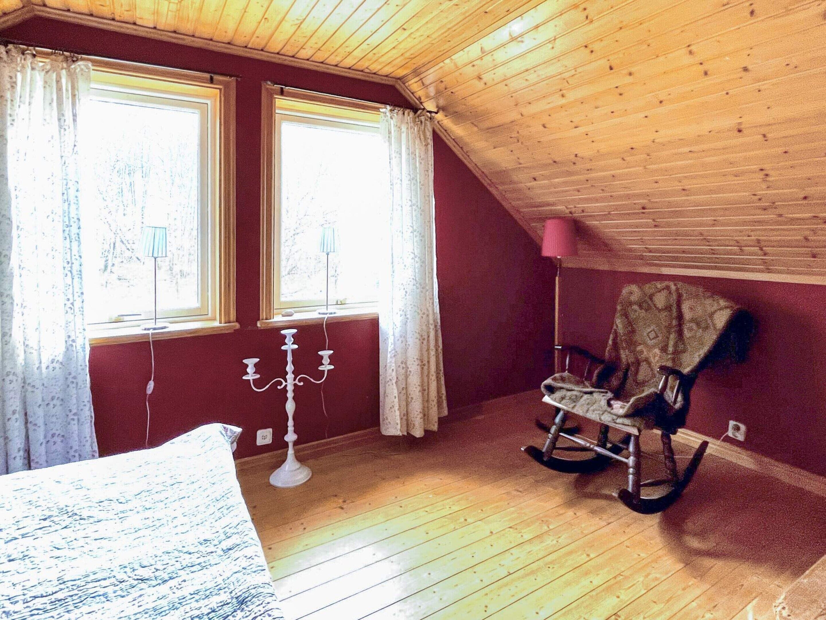 A room with wooden flooring, two windows with curtains, a rocking chair, and a candelabra.