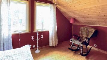 A room with wooden flooring, two windows with curtains, a rocking chair, and a candelabra.