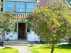A building with a wooden door, a small porch, and a tree with pink flowers.
