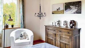 A bedroom with a bed, a white armchair, a wooden dresser, a chandelier, and two framed pictures on the wall. - 4 Star Holiday Home in Onsala (Gottskar)