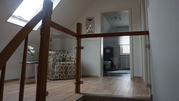 A spacious room with a wooden staircase, a patterned sofa, and a view of a kitchen through an open door. - Elisabeth on the Loreley (Sankt Goar)