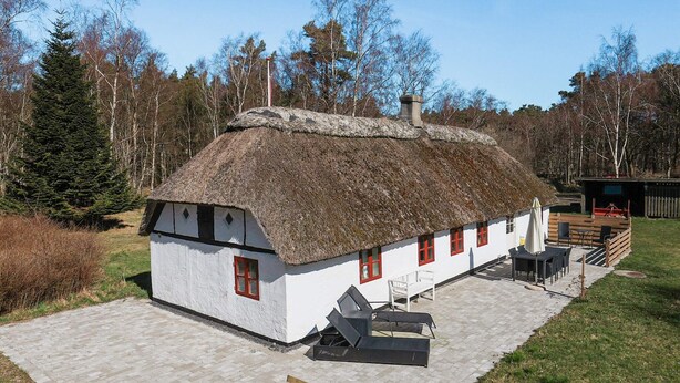 A thatched-roof house with a white exterior, a small deck, and a wooden bench.