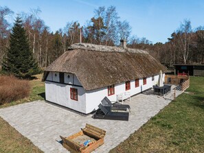 A thatched-roof house with a white exterior, a small deck, and a wooden bench.