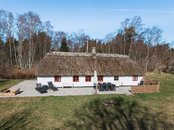 A white cottage with a thatched roof, a patio with outdoor furniture, and a wooden deck.