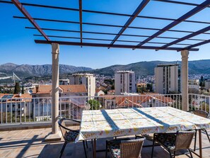 A terrace with a table and chairs, overlooking a cityscape with mountains in the background. - Apartment Dorica - Two Bedroom Apartment With Terrace (Dubrovnik)
