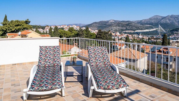A rooftop terrace with two sun loungers, a small table, and a view of a cityscape and mountains. - Apartment Dorica - Two Bedroom Apartment With Terrace (Dubrovnik)