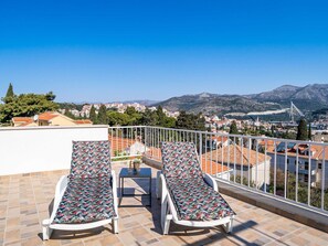 A rooftop terrace with two sun loungers, a small table, and a view of a cityscape and mountains. - Apartment Dorica - Two Bedroom Apartment With Terrace (Dubrovnik)