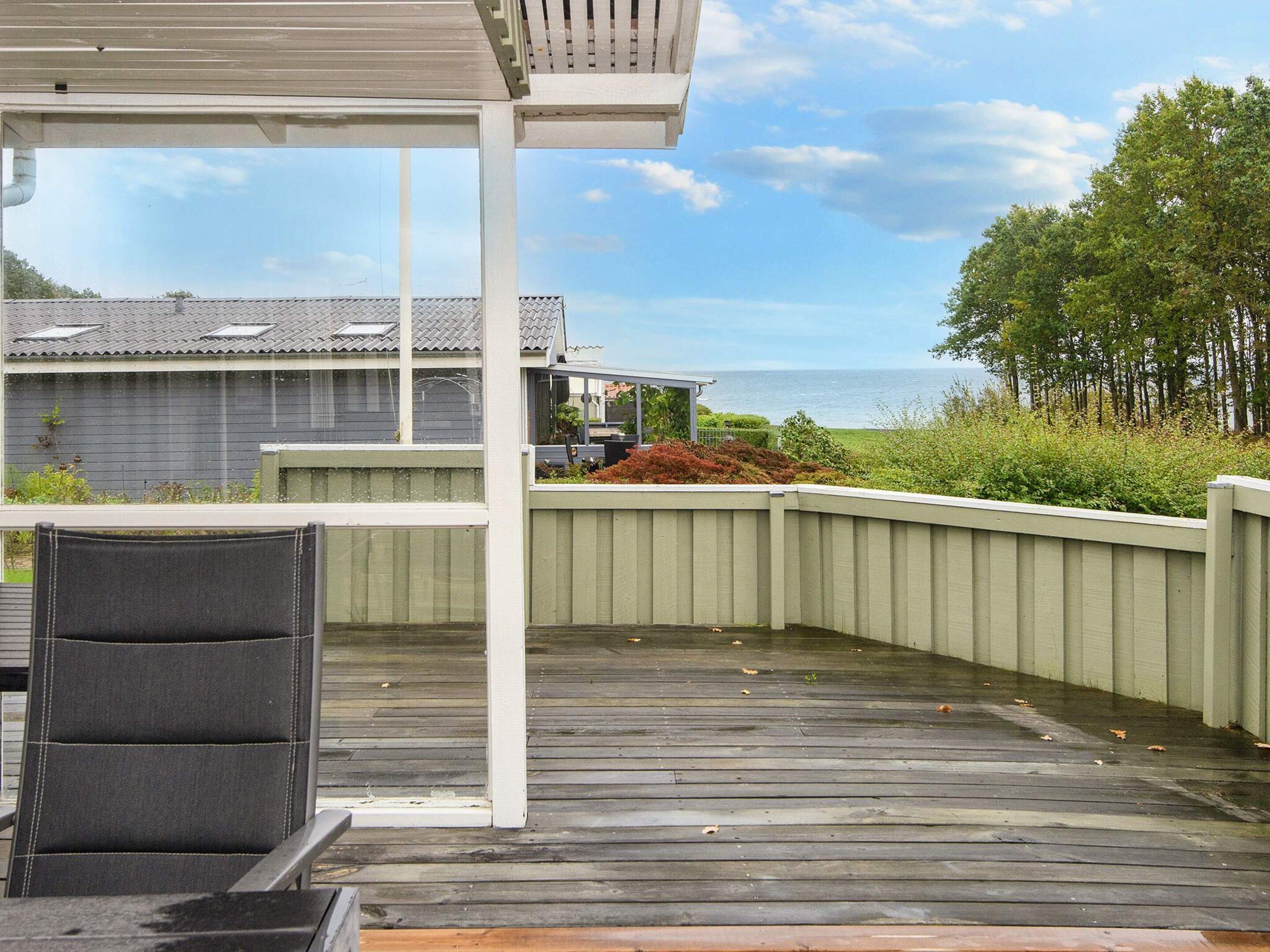 A wooden deck with a covered seating area, overlooking a body of water and a residential building.