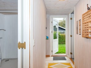 A hallway with a wooden door leading to a garden, a mat at the entrance, and a shelf with decorative items. - 5 Person Holiday Home in Juelsminde (Horsens)