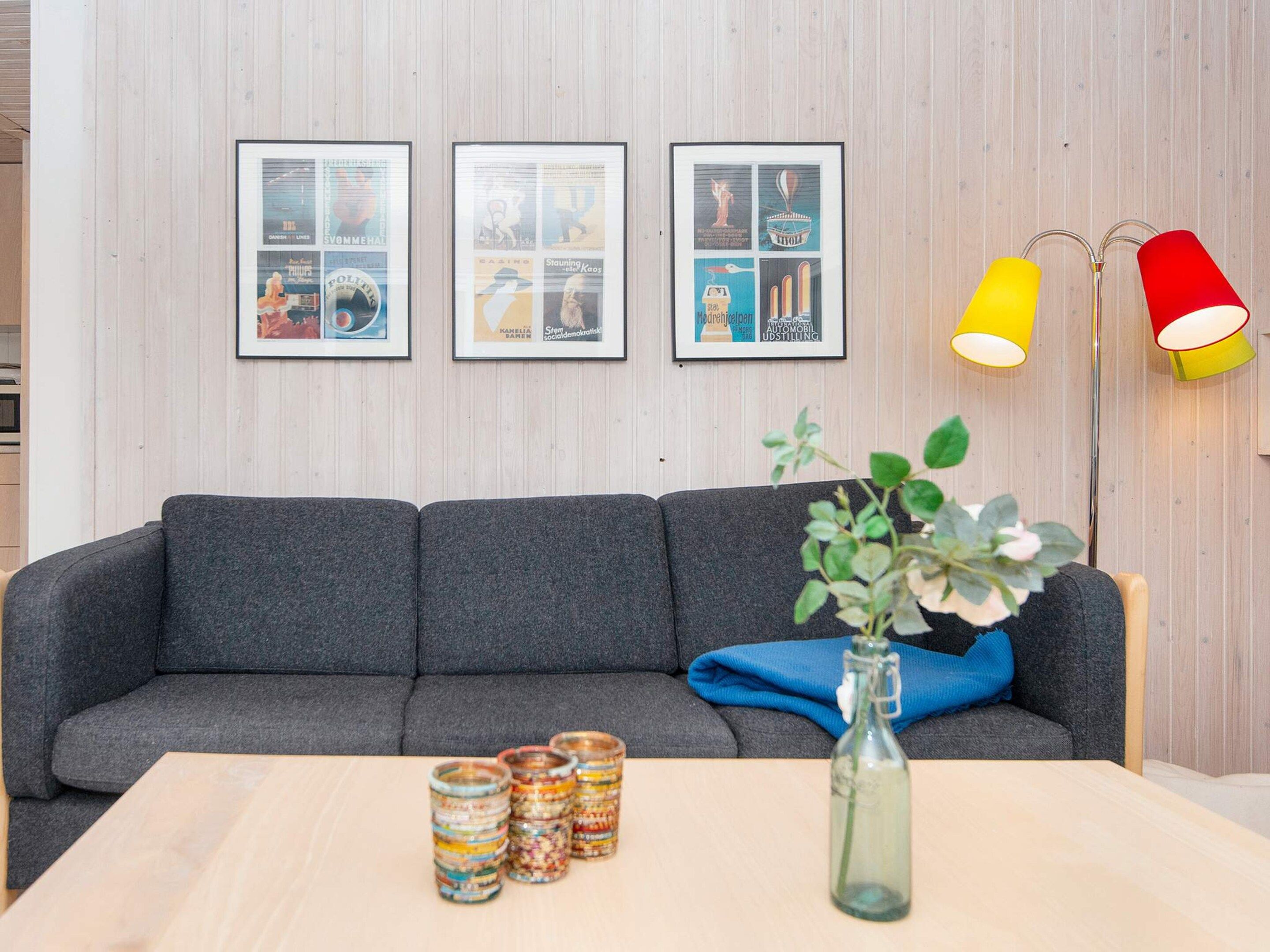 A modern living room with a grey sofa, a wooden coffee table, and a vase with a plant. There are framed pictures on the wall and two floor lamps.