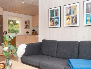 A living room with a grey sofa, a small table with a vase of flowers, and framed posters on the wall. - 5 Person Holiday Home in Juelsminde (Horsens)
