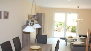 Un coin repas avec une table en bois, des chaises et des luminaires suspendus. Une porte-fenêtre coulissante donne accès à un patio extérieur.