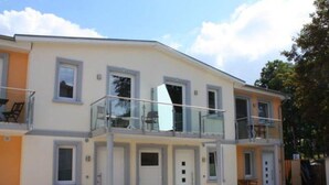 Un bâtiment à deux étages doté de balcons, d’un toit plat et d’un petit jardin.