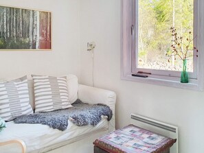 A room with a white sofa, a small table, a window with a view of trees, and a painting on the wall. - 6 Person Holiday Home in Blido (Blidö)