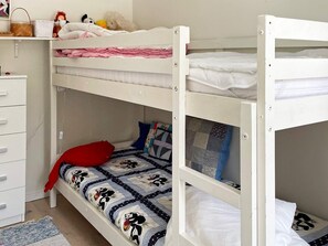 A bunk bed room with a white dresser, a red pillow, and a quilted bedspread.