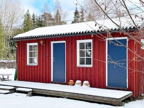 A red wooden cabin with two blue doors and windows, a small porch, and a snow-covered roof. - 6 Person Holiday Home in Blido (Blidö)