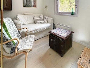 A cozy room with a white sofa, a patterned armchair, a small wooden table, and a radiator. - 6 Person Holiday Home in Blido (Blidö)