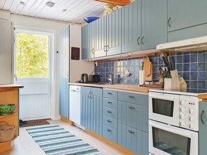 A kitchen with blue cabinets, a wooden countertop, a stove, and a window with a view of greenery. - 6 Person Holiday Home in Blido (Blidö)