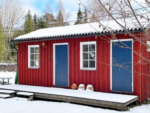 A red wooden cabin with two blue doors and windows, a small porch, and a snow-covered ground.