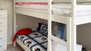 Une chambre avec un lit superposé, une commode blanche, un oreiller rouge et une couvre-lit matelassée.