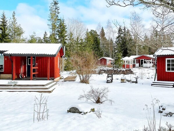 A cluster of red cabins with snow-covered roofs, surrounded by trees and a clear sky. - 6 Person Holiday Home in Blido (Blidö)