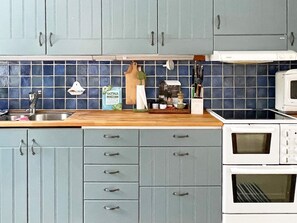 A kitchen with blue cabinets, a wooden countertop, a sink, a microwave, and a stove.