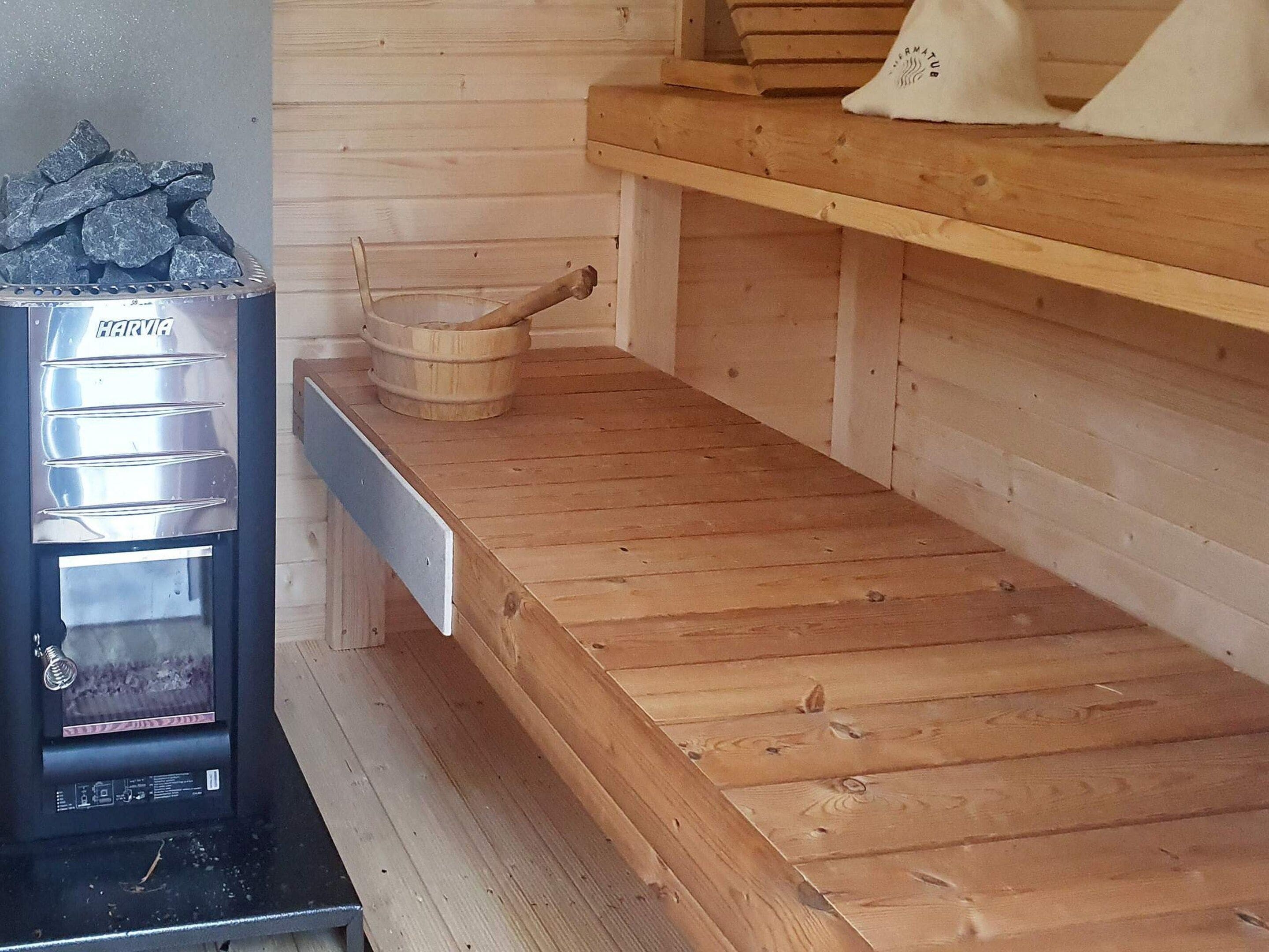 A sauna with a Harvia stove, a wooden bench, and a wooden shelf.