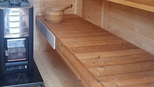 Un sauna équipé d’un poêle Harvia, d’un banc en bois et d’une étagère en bois.