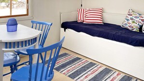 A room with a bed, a table with chairs, a window with a view of trees, and shelves with various items. - 6 Person Holiday Home in Blido (Blidö)