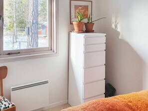 A room with a window, a radiator, a white storage unit, and a plant on the windowsill.