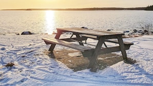 A wooden picnic table on a snowy shore with a body of water and a distant shoreline in the background. - 6 Person Holiday Home in Blido (Blidö)