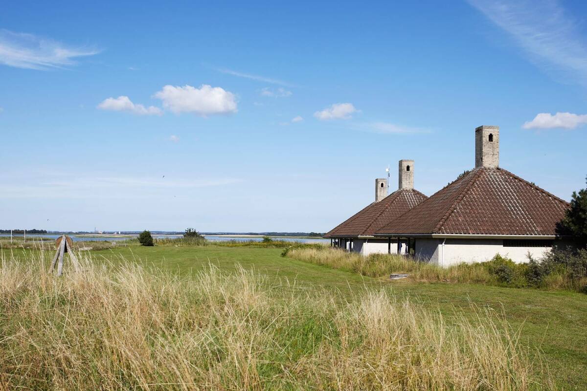 A traditional building with a tiled roof and chimneys, situated in a grassy field with a clear sky.
