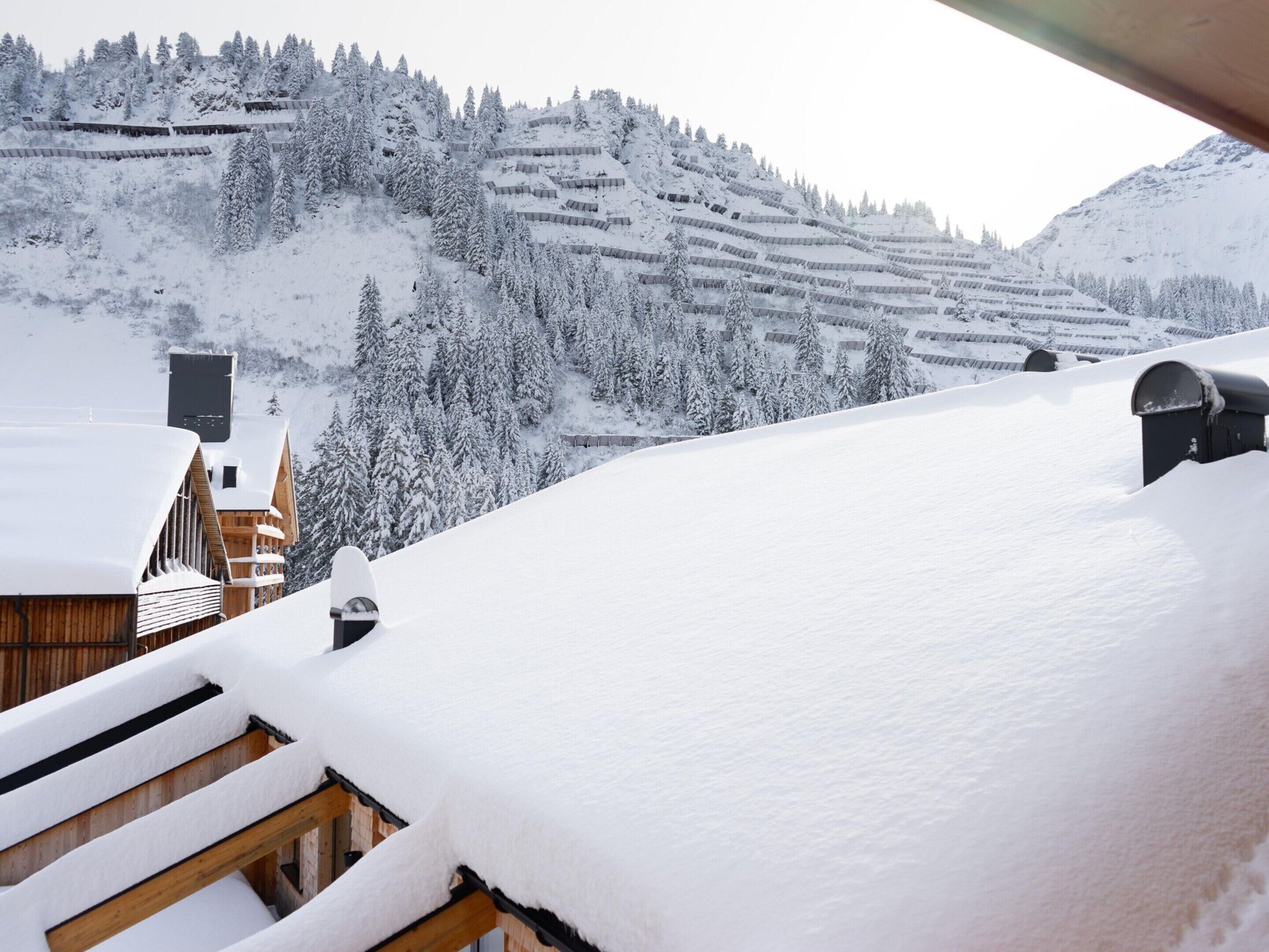 Un paysage montagneux enneigé avec un bâtiment en bois et un toit recouvert de neige.