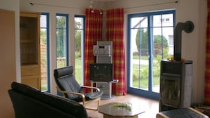 A living room with a fireplace, a television, and a dining area with a table and chairs. - Holiday Home Der Schwelmer (Zingst)