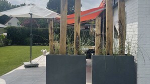 Un patio con sombrilla blanca, pilares de madera y pared de ladrillo blanco.
