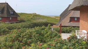 Huisjes met rieten daken en bakstenen muren, omgeven door weelderige begroeiing en uitzicht op zee.
