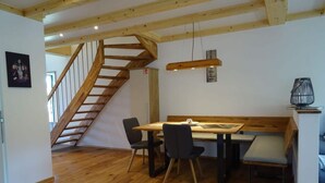 Un comedor con una mesa y sillas de madera, un banco, una escalera y una lámpara colgante.