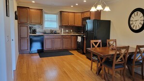 A kitchen with wooden cabinets, a black refrigerator, a dining table with chairs, and a wall clock.