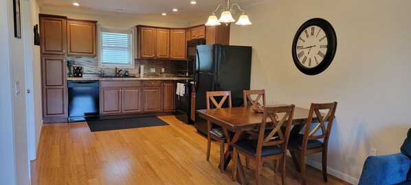 A kitchen with wooden cabinets, a black refrigerator, a dining table with chairs, and a wall clock.