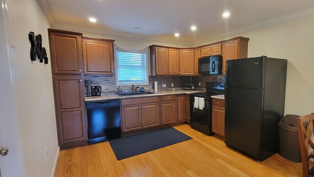 A compact kitchen with wooden cabinets, a black refrigerator, a microwave, and a dishwasher.