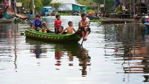 A group of people in a green boat on a calm water body, surrounded by floating houses and greenery. - Siem Reap Homesteading Garden Retreat (Siem Reap)