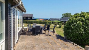 Une terrasse avec des meubles d’extérieur, une haie et une vue sur la mer.