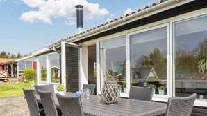 Un espace extérieur abrité, aménagé pour prendre les repas, avec une table et des chaises, de grandes fenêtres et une cheminée.