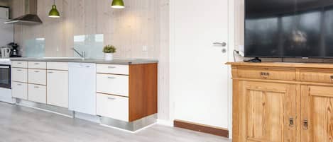 A modern kitchen with wooden cabinets, a built-in oven, and a large TV on a wooden cabinet.