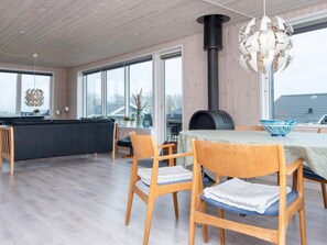 A modern kitchen with a large window, a built-in stove, and a dining area with wooden chairs and a table. - 7 Person Holiday Home in Juelsminde (Horsens)