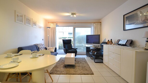 A modern living room with a dining table, sofa, TV, and kitchen area. - Apartment Oostduinkerke Near Beach and Dunes (Koksijde)