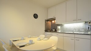 Ett modernt kök med vita skåp, en bänkskiva i granit och en matplats med ett bord för fyra personer.