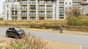 En modern lägenhetsbyggnad med flera balkonger och en parkeringsplats framför.
