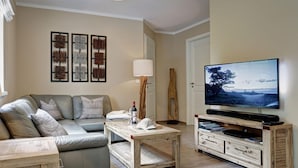 A living room with a sofa, coffee table, TV stand, and artwork on the wall. - Beach Idyll Holiday Apartment (Ostseebad Baabe)